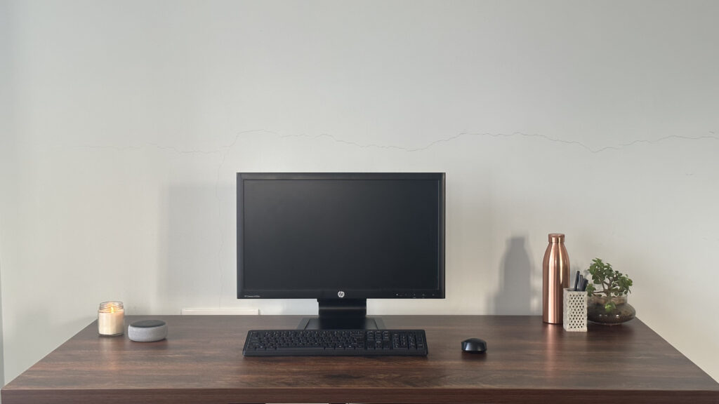 Computer, bottle, plant, candle, pencil stand on a table